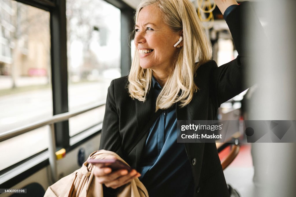 Happy businesswoman with smart phone travelling in bus