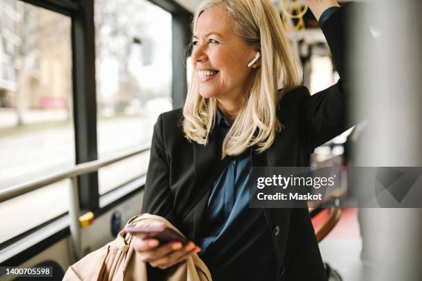 happy businesswoman with smart phone travelling in bus - in ear headphones stock pictures, royalty-free photos & images