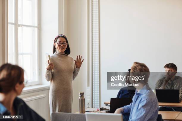 smiling female teacher gesturing while teaching students in classroom - female professor stock pictures, royalty-free photos & images