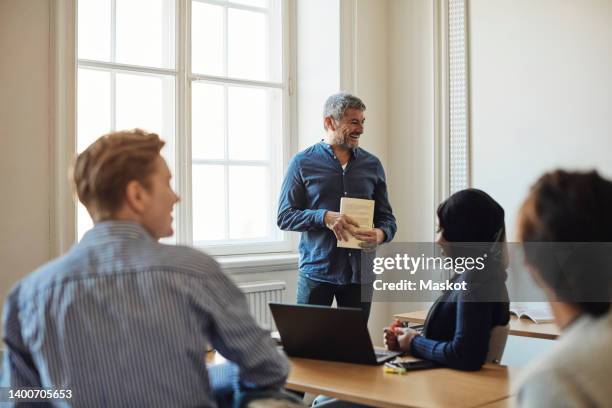 smiling male professor with book standing in classroom - white male professor foto e immagini stock