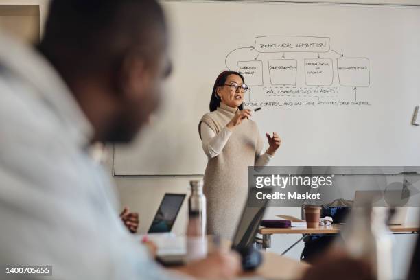 female teacher gesturing while explaining diagram on whiteboard in classroom - expositor fotografías e imágenes de stock