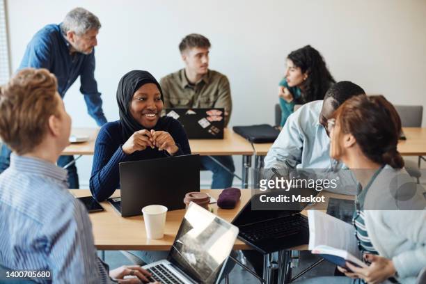 smiling female student discussing with friends while sitting in classroom - student stockfoto's en -beelden