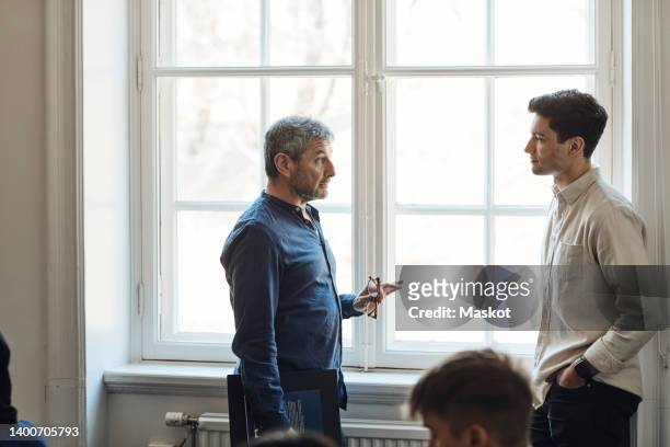 male professor talking with student near window in university - white male professor foto e immagini stock
