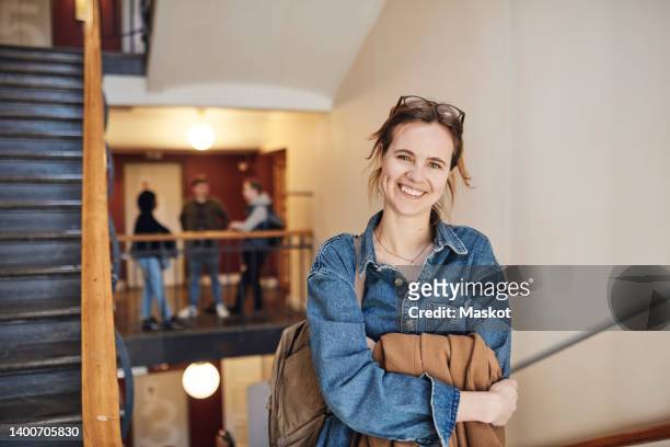 portrait of happy female student with arms crossed standing at staircase in university - school scandinavia stock pictures, royalty-free photos & images