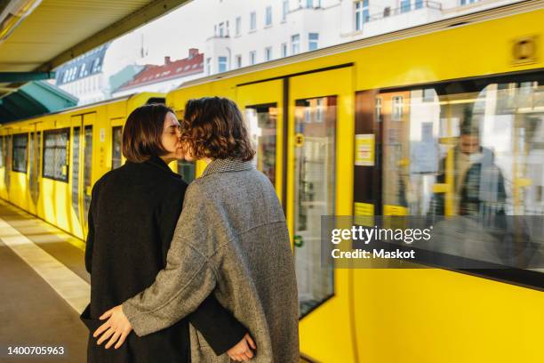 lesbian couple kissing while standing by yellow train at railroad station - lgbtqi menschen stock-fotos und bilder