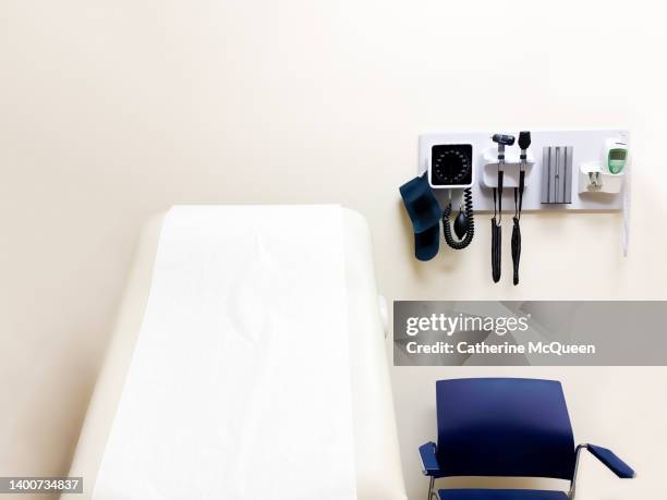 access to medical care: wall-mounted medical diagnostic equipment beside standard patient examination chair - sala di consultazione medica foto e immagini stock