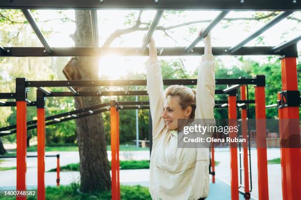 young woman climbing on monkey bars in sunny morning. - reck stock-fotos und bilder