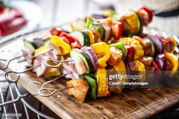 pile of skewers with chicken meat, bacon, and vegetables such as corn, peppers, onions is ready to be put on a barbeque. - chicken skewers stockfoto's en -beelden