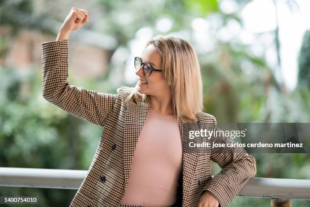 a happy and proud young woman shows off her biceps, women in business, girl power concepts - honors show stock pictures, royalty-free photos & images