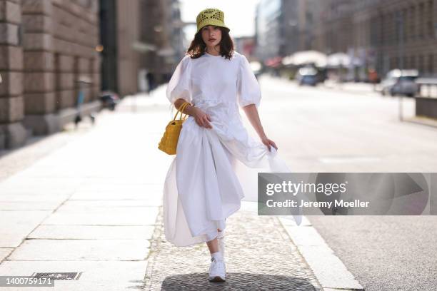 Lena Naumann wearing New Balance x Miu Miu white sneaker, Cecilie Bahnsen white maxi dress, Prada kiwi green bucket hat, Prada yellow bag on May 31,...