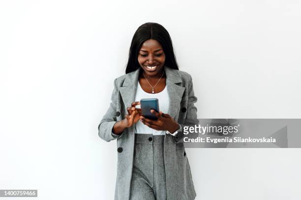 beautiful young black woman using phone against white wall background. - model business woman stock-fotos und bilder