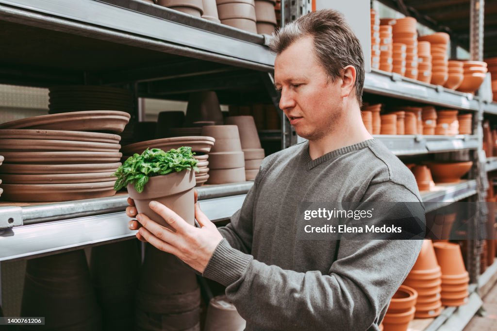 A male gardener chooses a pallet for a home flower in a flower shop or mall. Gardening at home as a hobby for men. Home gardening