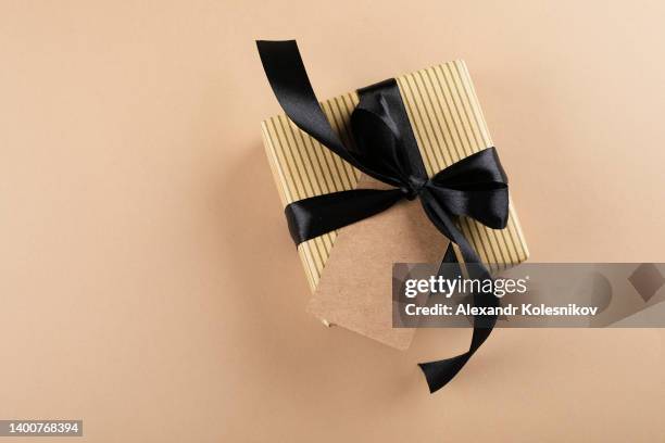 top view gift box with empty label and black ribbon on beige background with copy space. happy father's day, birthday concept - verjaardagskado stockfoto's en -beelden