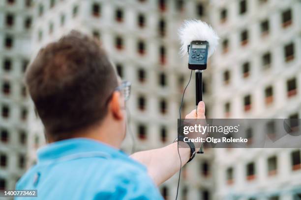 rearview of mature dark-haired man checking sound volume by microphone, audiometer in urban city center - loud man imagens e fotografias de stock