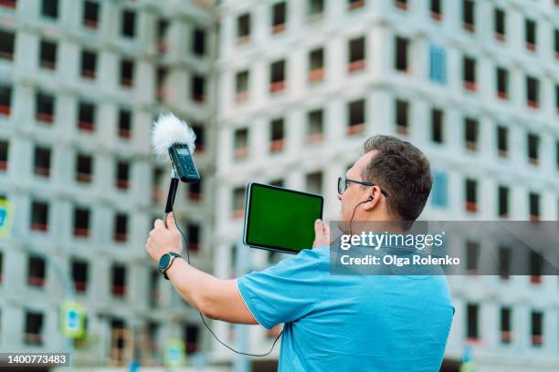 concentrated mature man in glasses checking sound volume, examining sound level by  dictaphone recorder and  digital tablet against building - 小型テープレコーダー ストックフォトと画像