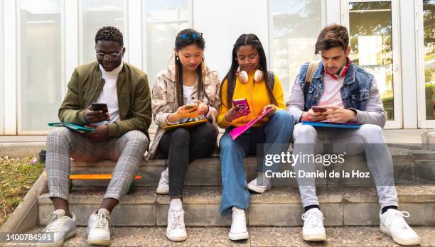 group of multiracial teenage college friend students ignoring each other looking at mobile phone. smartphone addiction. - celular escola imagens e fotografias de stock