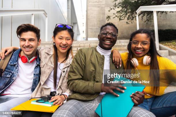 happy and smiling group of multiracial college student friends looking at camera sitting on stairs outside university building. - 交換留学生 ストックフォトと画像