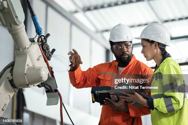 intelligent design of robotic welding process parameters in manufacturing industry. a female manufacturing process engineer and a welder is discussion in-front of a robotics welding in production line about welding process parameter to improve auto part. - protective workwear for manual worker stockfoto's en -beelden