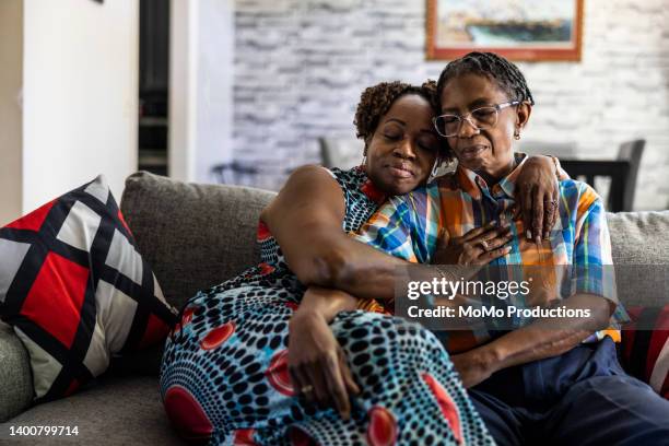 lesbian couple embracing on couch in their living room - gay seniors fotografías e imágenes de stock