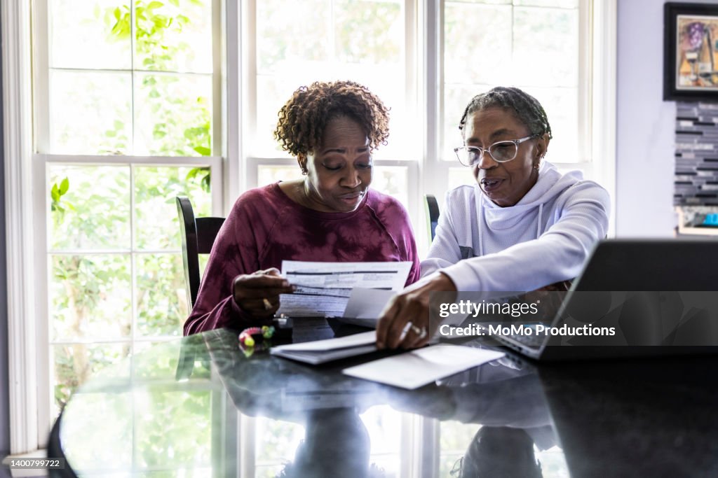 Lesbian couple paying bills and using laptop at kitchen table