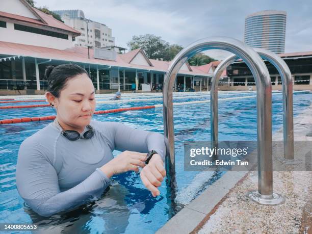 asian chinese female swimmer checking on her smart watch fitness tracker after swimming at pool side - woman swimsuit happy normal stock pictures, royalty-free photos & images