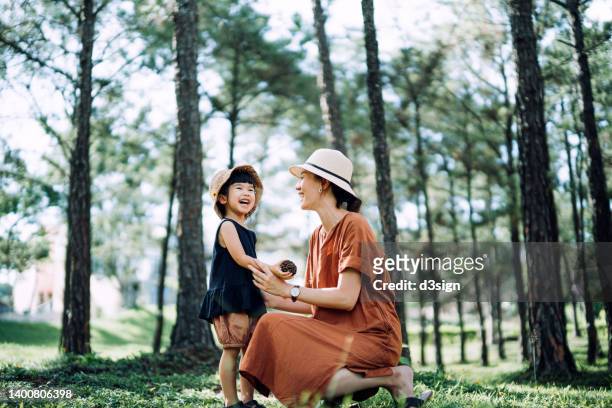 loving young asian mother relaxing with her little daughter in the woods, chatting and smiling joyfully, against beautiful sunlight. precious moment between mother and daughter. family lifestyle. family love and care. exploring in nature and outdoor fun - sonnenhut pflanzengattung stock-fotos und bilder