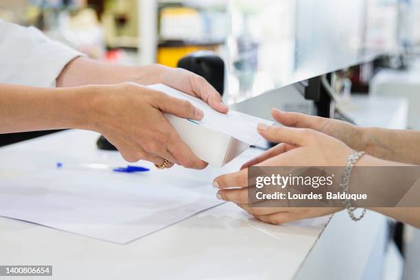 pharmacist handing a box of medicine to a customer in a pharmacy - farmacia fotografías e imágenes de stock