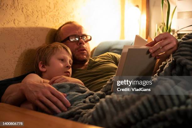 father reading a book to son - bedtime stockfoto's en -beelden