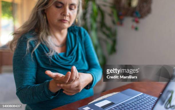 overworked mature woman with gray hair and wrist pain working on laptop from home, carpal tunnel syndrome - carpaletunnelsyndroom stockfoto's en -beelden