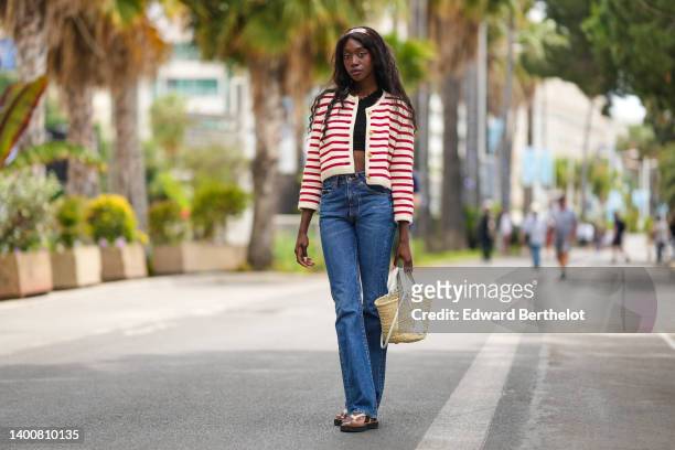 Emmanuelle Koffi wears a Celine full look, a headband, a red and white stripe jacket, a black crop top / tank top, blue denim flare jeans / pants, a...