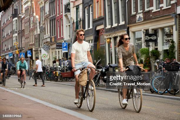 einkaufsstraße mit fahrradfahrern auf dem haarlemmerdijk bei sommersonnenuntergang, amsterdam - amsterdam bike stock-fotos und bilder