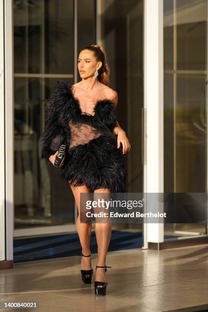 Maja Malnar wears jewelry, diamond bejeweled earrings, a black mini one shoulder dress with fluffy parts and see-through sheer fabric, a glitter...