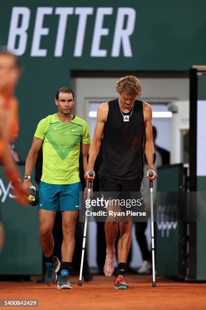 Alexander Zverev of Germany walks back out to the court on crutches with Rafael Nadal of Spain following an injury against Rafael Nadal of Spain...