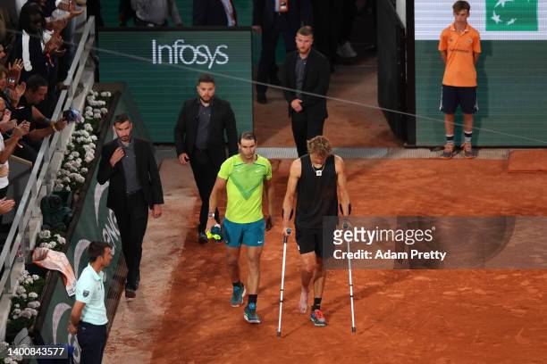 Alexander Zverev of Germany walks back out to the court on crutches with Rafael Nadal of Spain following an injury against Rafael Nadal of Spain...