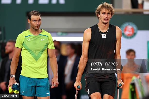 Alexander Zverev of Germany walks back out to the court on crutches with Rafael Nadal of Spain following an injury against Rafael Nadal of Spain...