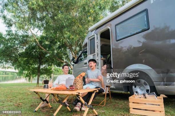 playful mother carrying boy at camper van in woodland - asian family camping stock pictures, royalty-free photos & images