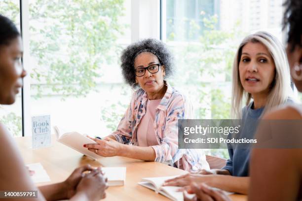 diverse women listen to unrecognizable book club leader - book club meeting stock pictures, royalty-free photos & images