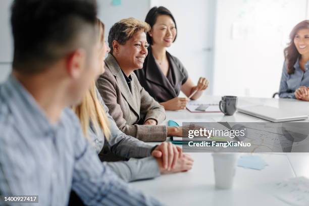 multiracial mature woman attends meeting with multiracial group of colleagues in creative office interior - community college stockfoto's en -beelden