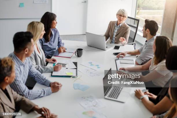 mujer de negocios senior con un grupo de colegas de trabajo multirraciales que discuten ideas y negocios juntos sentados a la mesa en el interior de la oficina creativa moderna vista de alto ángulo durante el día - corporate hierarchy fotografías e imágenes de stock