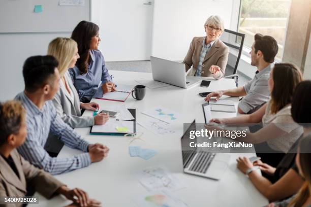 senior businesswoman with group of multiracial work colleagues discussing ideas and business together sitting at table in modern creative office interior high angle view daytime - hierarquia de corporação imagens e fotografias de stock