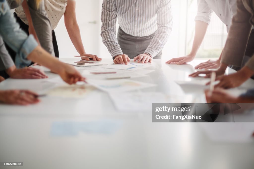 Low angle view of hands of multiracial group of people working with ideas and brainstorming together to make decisions with documents on table in creative office teamwork