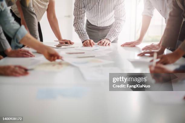 low angle view of hands of multiracial group of people working with ideas and brainstorming together to make decisions with documents on table in creative office teamwork - idee stockfoto's en -beelden