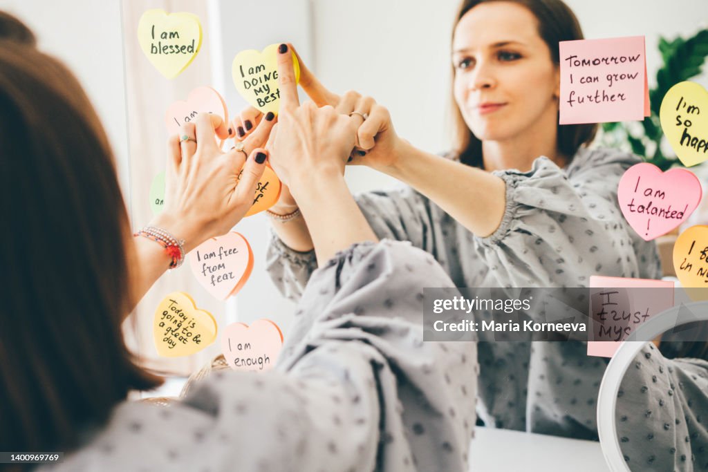 Woman stick a sticker with affirmations on the mirror.