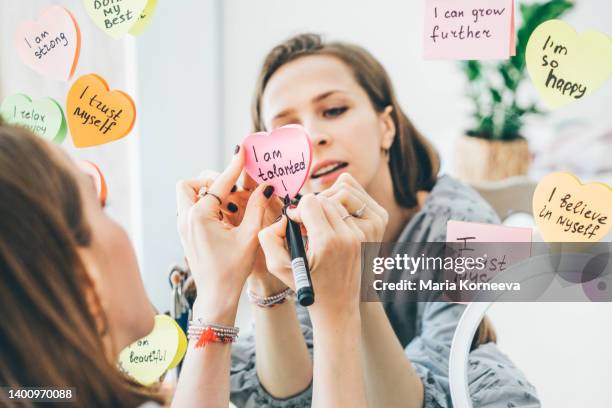 woman writing affirmations on a sticker near the mirror. - best script stock pictures, royalty-free photos & images