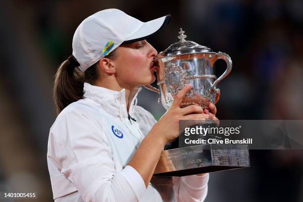 Iga Swiatek of Poland kisses the trophy as the colours of the Ukraine flag are seen on their cap after winning against Coco Gauff of The United...