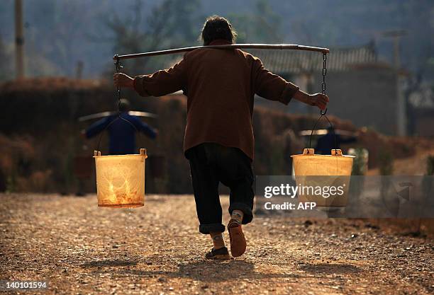 Chinese villagers carry pails of water they collected from a well, back to their homes in Yiliang, southwest China's Yunnan province on February 27,...