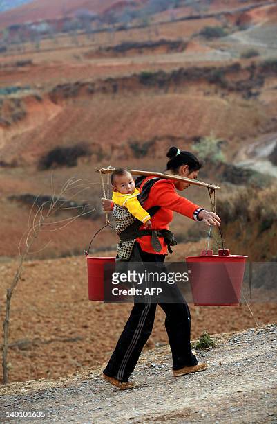 Chinese woman, with her child on her back, carries pails of water she collected from a well, back to her home in Yiliang, southwest China's Yunnan...
