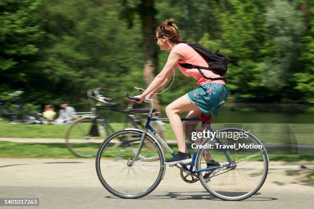 woman cycling in urban park on a summer day, vondelpark, amsterdam - rugzak stock pictures, royalty-free photos & images