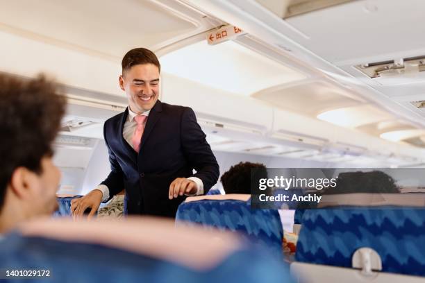 male cabin crew member walks down the aisle checking on passengers - tripulação imagens e fotografias de stock