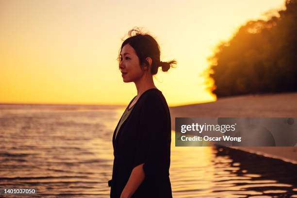 sideview of young woman standing on the beach at sunset. enjoying golden hour. summer vacation. beach holiday. - young woman standing against clear sky ストックフォトと画像